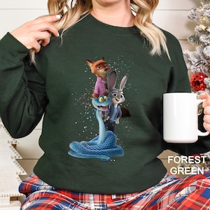 Peut inclure: Sweat-shirt vert for&ecirc;t avec un motif des personnages du film d'animation Zootopie. Le motif comprend Nick Wilde, Judy Hopps et un serpent bleu. Le sweat-shirt est de couleur unie avec les mots "Forest Green" imprim&eacute;s en bas &agrave; droite.