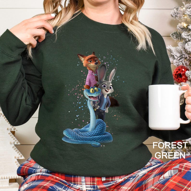 Peut inclure: Sweat-shirt vert for&ecirc;t avec un motif des personnages du film d'animation Zootopie. Le motif comprend Nick Wilde, Judy Hopps et un serpent bleu. Le sweat-shirt est de couleur unie avec les mots "Forest Green" imprim&eacute;s en bas &agrave; droite.
