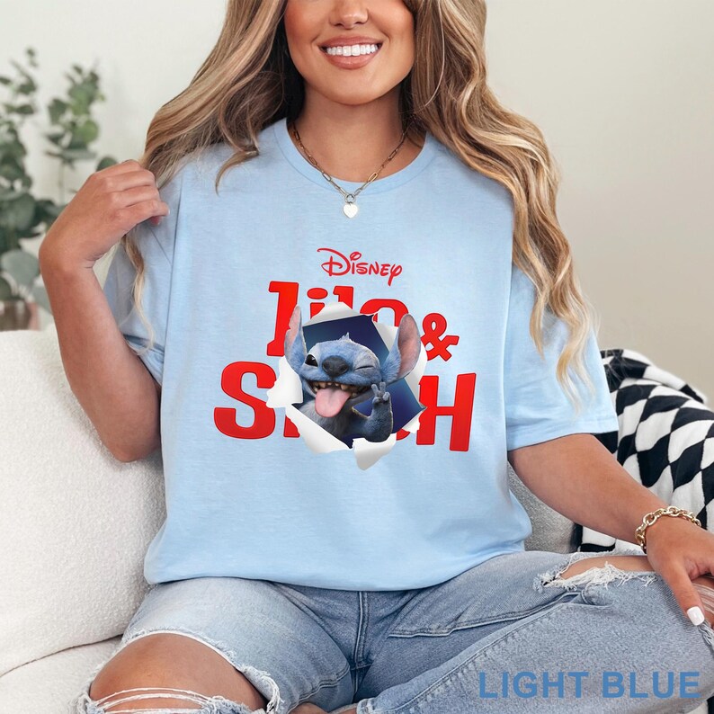 Puede incluir: Camiseta azul claro con el personaje de Disney Stitch rompiendo un efecto de papel rasgado. El texto "Disney" est&aacute; encima de la imagen, con "Stitch" en rojo debajo. La camiseta es de color azul claro.
