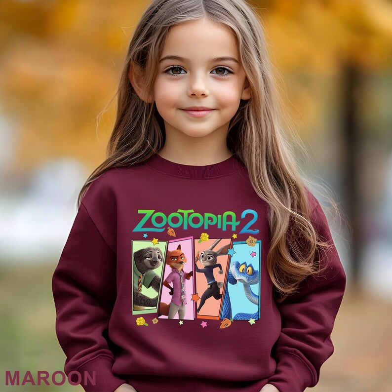 May include: A maroon sweatshirt with the text "ZOOTOPIA 2" and cartoon characters from the movie. The design includes a sloth, fox, rabbit, and snake. The word "MAROON" is printed at the bottom of the sweatshirt.