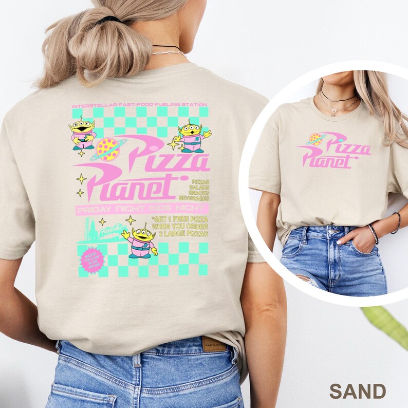 May include: Sand-colored t-shirt featuring the text "Pizza Planet" in pink, with a graphic of a pizza slice. The back of the shirt has a larger design with alien characters and the words "Pizza Planet" and "Friday Night Kids Night."