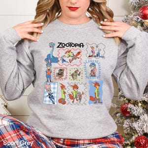 May include: Sport Grey sweatshirt featuring a colorful graphic of characters from the animated film "Zootopia." The design includes the film's title and various character illustrations within decorative frames. The sweatshirt is a comfortable, casual style.