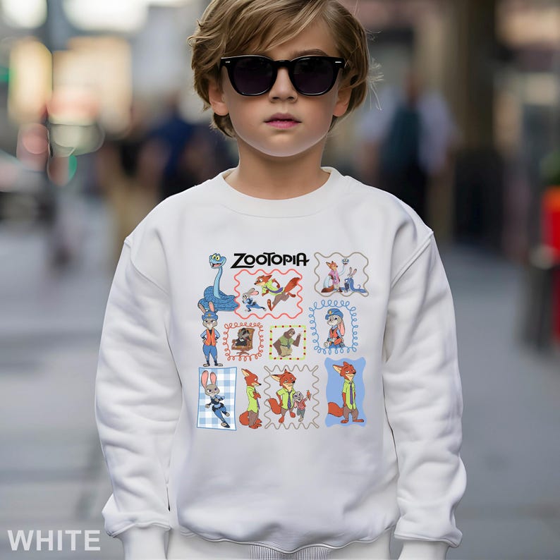 May include: White sweatshirt featuring the word "Zootopia" and cartoon character illustrations. The sweatshirt is a crew neck style and is made of a soft material. The design includes various characters from the animated movie.