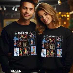 May include: Black sweatshirts featuring a colorful graphic design from the movie "Zootopia." The design includes various characters in framed illustrations, with the word "Zootopia" at the top. The sweatshirts are worn by two people.