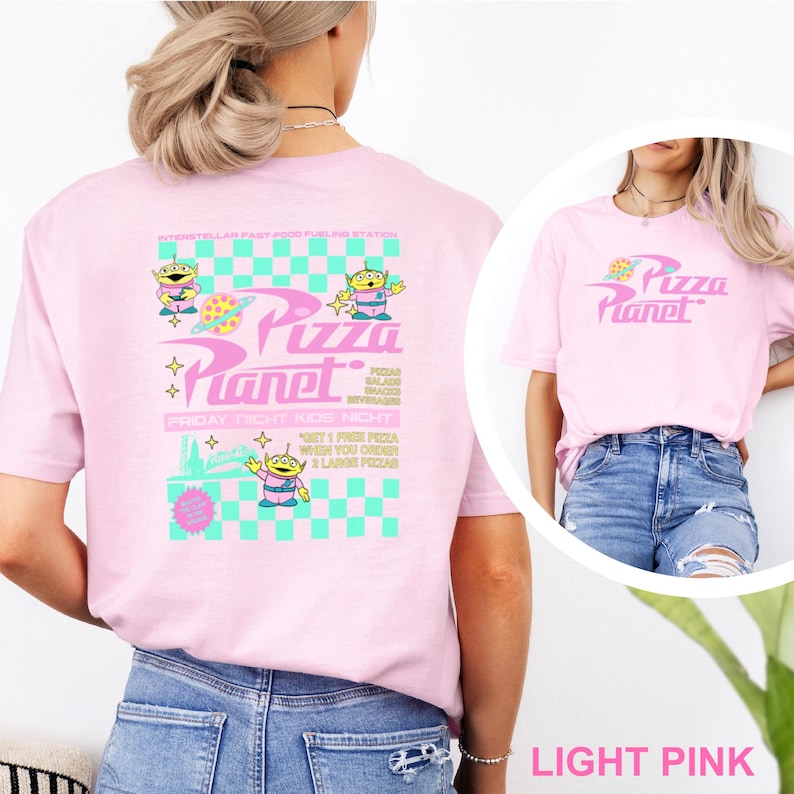 May include: Light pink t-shirts with the Pizza Planet logo and graphics. One shirt features the logo on the front, while the other has a larger design on the back with alien characters and text. The shirts are made of a soft material.