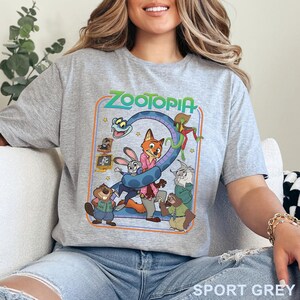 Pode incluir: Camiseta cinza desportiva com um design gr&aacute;fico colorido do filme de anima&ccedil;&atilde;o Zootopia. O design inclui o t&iacute;tulo do filme e v&aacute;rios personagens animais. A camiseta &eacute; feita de material macio.