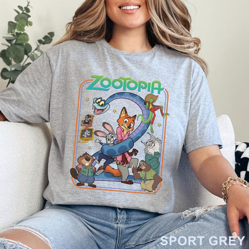Pode incluir: Camiseta cinza desportiva com um design gr&aacute;fico colorido do filme de anima&ccedil;&atilde;o Zootopia. O design inclui o t&iacute;tulo do filme e v&aacute;rios personagens animais. A camiseta &eacute; feita de material macio.