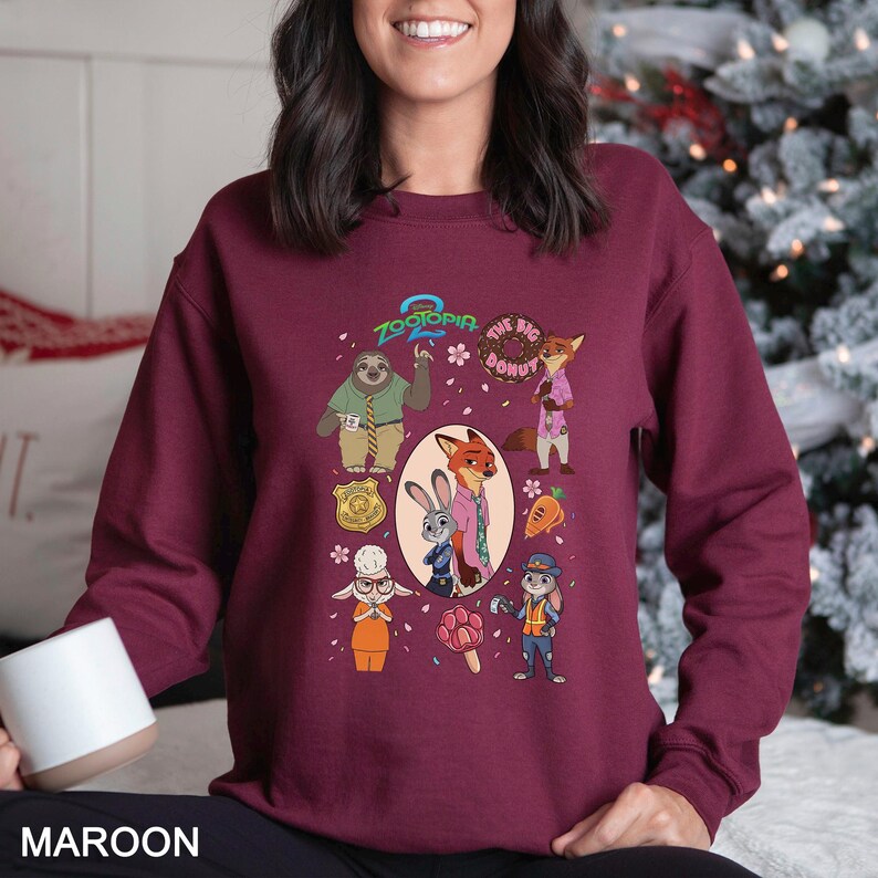 May include: Maroon sweatshirt featuring characters from the animated film Zootopia. The design includes images of a sloth, fox, rabbit, and other characters, along with the text "Zootopia" and "The Big Donut".
