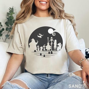 Pu&ograve; includere: T-shirt color sabbia con grafica nera dei personaggi di "Nightmare Before Christmas" su sfondo circolare scuro con luna piena. La parola "SAND" &egrave; stampata in basso sulla maglietta.