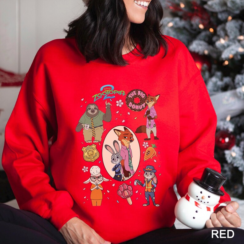 May include: A red sweatshirt featuring characters from the animated film "Zootopia." The design includes Judy Hopps, Nick Wilde, and other characters, along with the text "Zootopia" and "The Big Donut."