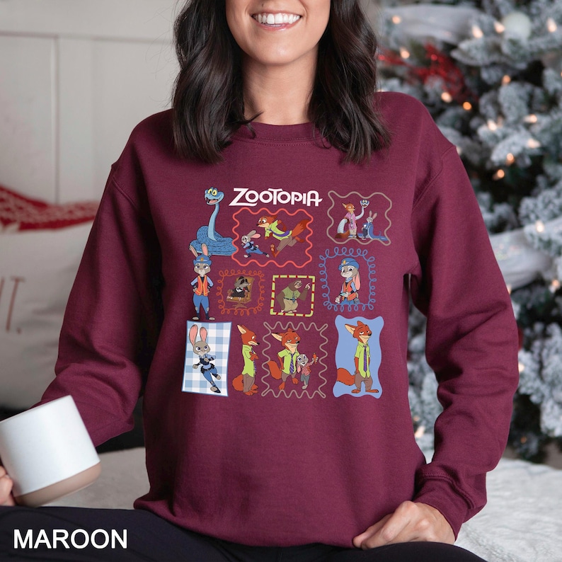 May include: Maroon sweatshirt featuring the word "Zootopia" above a grid of cartoon character images. The sweatshirt has a crew neck and long sleeves. The word "MAROON" is printed at the bottom of the image.