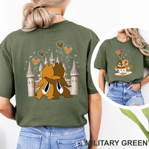 May include: Military green t-shirt featuring a cartoon graphic of two chipmunks hugging in front of a castle. The back of the shirt shows the chipmunks hugging in front of a castle. The front of the shirt shows the chipmunks in a teacup with balloons.