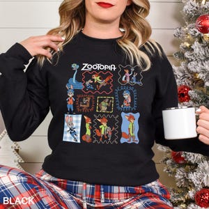 May include: Black crewneck sweatshirt featuring a colorful graphic of characters from the animated film "Zootopia." The design includes the film's title and various character illustrations framed in different styles. The word "BLACK" is printed at the bottom.