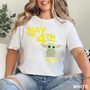 May include: White t-shirt with a yellow graphic that says "May the 4th Be With You" and a green Baby Yoda character. The year 2025 is printed below the character.