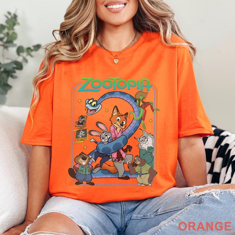 Pode incluir: Camiseta laranja vibrante com um gr&aacute;fico colorido do filme "Zootopia". O design inclui o t&iacute;tulo e v&aacute;rios personagens animais. A camiseta &eacute; feita de um material macio.