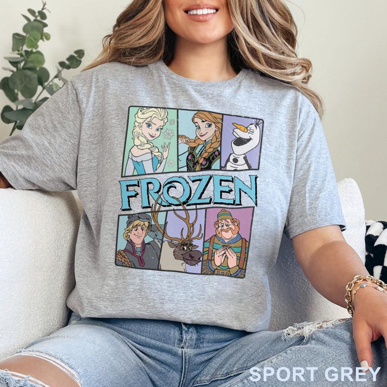 May include: Sport grey t-shirt featuring a colorful graphic of characters from the movie "Frozen." The design includes Elsa, Anna, Olaf, Kristoff, Sven, and Hans. The word "FROZEN" is printed in large, light blue letters.