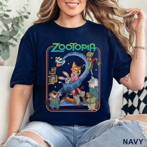 Pode incluir: Camiseta azul marinho com um gr&aacute;fico colorido de "Zootopia". O design apresenta personagens como Judy Hopps e Nick Wilde, juntamente com o t&iacute;tulo do filme. Uma pe&ccedil;a de roupa confort&aacute;vel e casual para os f&atilde;s do filme de anima&ccedil;&atilde;o.