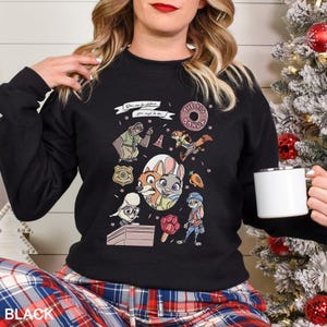 Może przedstawiać: Czarna bluza z okrągłym dekoltem z postaciami z kresk&oacute;wek i tekstem z filmu Zwierzogr&oacute;d. Projekt zawiera obrazy leniwca, lisa, kr&oacute;lika i innych postaci. Tekst brzmi "You can be whatever you wish to be" i "The Big Donut".