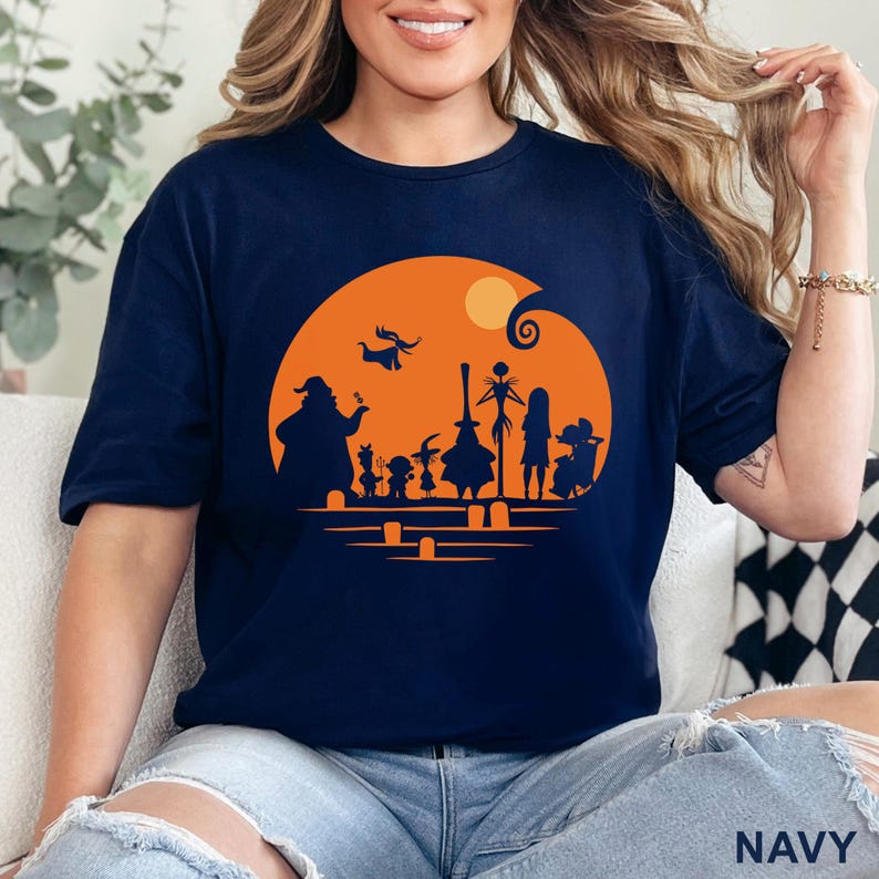 Pu&ograve; includere: T-shirt blu navy con grafica a tema Halloween. Il design include sagome di personaggi su uno sfondo arancione con una luna piena. La parola "NAVY" &egrave; stampata in basso sulla maglietta.