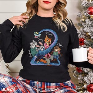 May include: Black sweatshirt with a cartoon illustration of animal characters, including a fox, rabbit, and beaver, with the names "Judy", "Nick", and "Nibbles". The graphic is in blue, pink, and brown. The word "BLACK" is at the bottom.