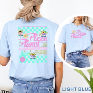 May include: Light blue t-shirt featuring the Pizza Planet logo and alien characters. The back of the shirt has a graphic with the text "Pizza Planet" and "Friday Night Kids Night". The shirt is made of a soft material.