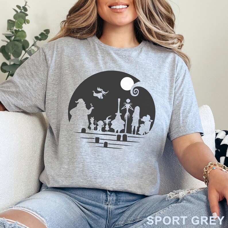 Pu&ograve; includere: T-shirt grigio sportivo con grafica in bianco e nero dei personaggi di The Nightmare Before Christmas. Il design include Jack Skellington, Sally e altre figure in una scena di cimitero. Il testo "SPORT GREY" &egrave; stampato in basso.