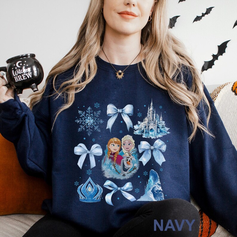 Puede incluir: Sudadera azul marino con un dise&ntilde;o de tem&aacute;tica invernal. El gr&aacute;fico incluye copos de nieve, lazos, un castillo e im&aacute;genes de Anna, Elsa y Olaf. La palabra "NAVY" est&aacute; impresa en la parte inferior. Una prenda c&oacute;moda e informal.