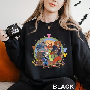 May include: Black crew neck sweatshirt with a colourful cartoon graphic of animal characters. The design includes a rainbow, flowers, and the word "BLACK" at the bottom. The sweatshirt is a crew neck style.
