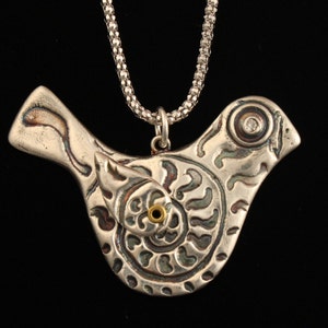 May include: A silver bird pendant necklace with intricate details and a small clear stone in the eye. The pendant is attached to a silver chain.