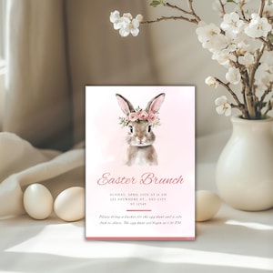 Op de afbeelding: Een roze en witte uitnodigingskaart met een aquarel-illustratie van een bruin konijn dat een roze bloemenkrans draagt. De tekst op de kaart luidt "Easter Brunch" en bevat de datum, tijd en locatie van het evenement. Er wordt ook vermeld dat je een emmer voor de eierenjacht en een bijgerecht om te delen mee moet nemen. De eierenjacht begint om 13:30 uur.