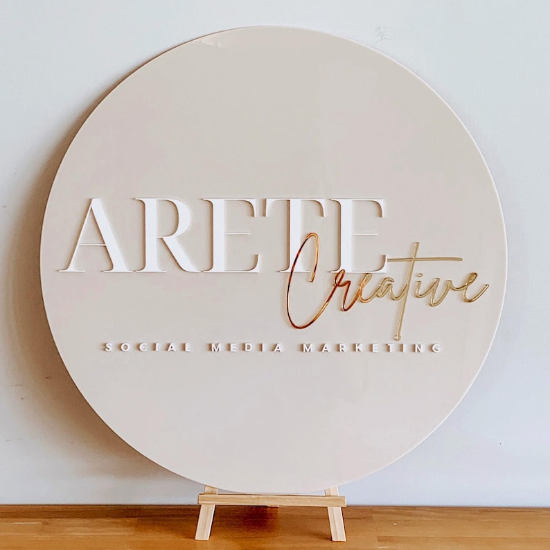 K&ouml;nnte beinhalten: Ein rundes, beiges Schild mit dem Text "ARETE Creative" in wei&szlig;er und goldener Schrift. Der Text "SOCIAL MEDIA MARKETING" ist ebenfalls in wei&szlig;er Schrift unter dem Haupttext.