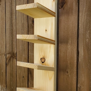 May include: A wooden wall shelf with four shelves. The shelves are made of light-colored wood and are attached to a vertical backing. The shelf is mounted on a wooden wall.