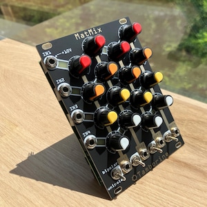 Peut inclure: Un module Eurorack noir avec le texte "MatMix" et "Q Tamborine" imprimé dessus. Le module possède quatre prises d'entrée étiquetées "IN1", "IN2", "IN3" et "IN4". Il possède également 16 boutons avec des boutons noirs, blancs, jaunes et orange. Le module possède deux interrupteurs à bascule étiquetés "unipolar" et "bipolar".