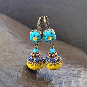 Peut inclure: Boucles d'oreilles pendantes au style vintage. Elles présentent des dessus turquoise en forme de fleur avec des centres jaunes, reliés à des gouttes en forme de cloche perlées jaunes et bleues. Les composants métalliques ont une finition bronze antique.