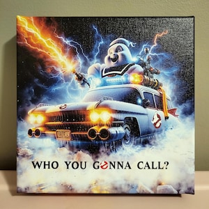 Può includere: Una stampa su tela nera con un'auto bianca dei Ghostbusters con un fantasma al volante. L'auto è circondata da fulmini e il testo "WHO YOU GONNA CALL?" è stampato in basso.