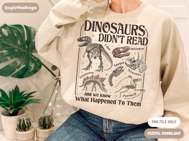 May include: Beige sweatshirt with a dinosaur-themed graphic. The graphic includes dinosaur skeletons and the text "DINOSAURS DIDN'T READ and we know What Happened To Them". The design features a T-Rex, Velociraptor, Triceratops, and other dinosaurs.