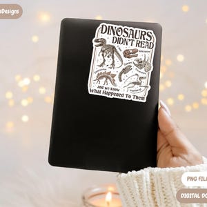 May include: A black electronic device with a sticker that reads "DINOSAURS DIDN'T READ" featuring dinosaur illustrations. The sticker also includes the text "and we know What Happened To Them". The image is a digital download.