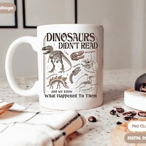 May include: White ceramic mug featuring a dinosaur-themed design with the text "DINOSAURS DIDN'T READ" and illustrations of various dinosaurs. The mug also includes the text "and we know What Happened To Them."