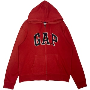 May include: A red zip-up hoodie with a hood and front pockets. The word "GAP" is across the chest in navy blue block letters with a white outline. The hoodie is made of a soft, comfortable material.