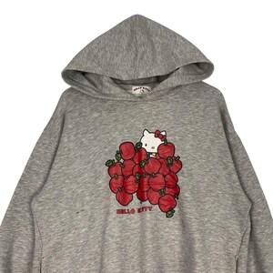 May include: Gray hooded sweatshirt with a Hello Kitty graphic. Hello Kitty is surrounded by red apples and the text "HELLO KITTY" is printed below the graphic.