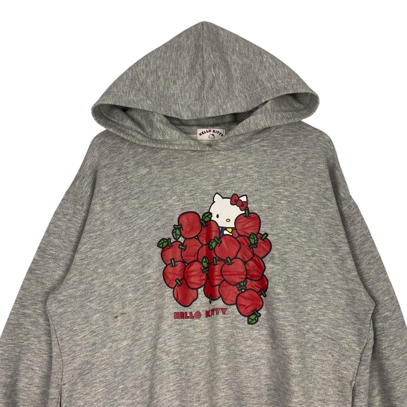 May include: Gray hooded sweatshirt with a Hello Kitty graphic. Hello Kitty is surrounded by red apples and the text "HELLO KITTY" is printed below the graphic.