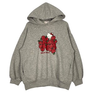 May include: A gray hooded sweatshirt with a Hello Kitty graphic. Hello Kitty is surrounded by red apples and the text "Hello Kitty" is printed below the graphic.