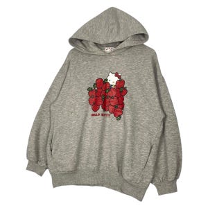 May include: A gray hooded sweatshirt with a Hello Kitty graphic. The graphic features Hello Kitty holding a bunch of red apples.