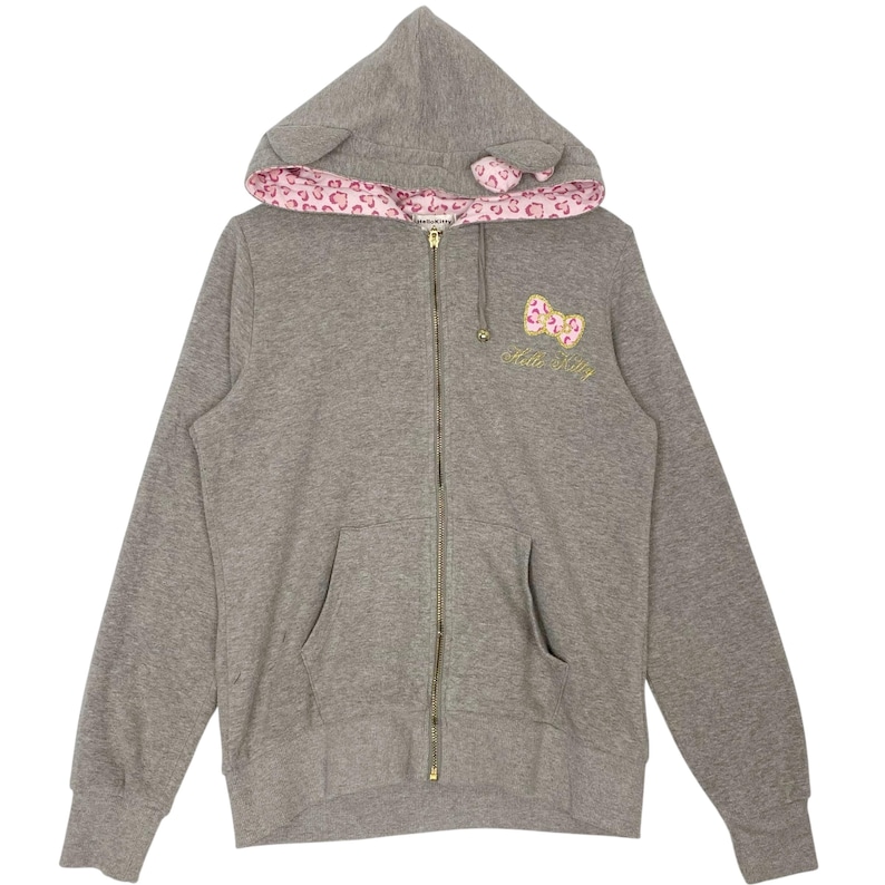 May include: Gray zip-up hoodie with a hood featuring cat ears and a pink leopard print lining. The front has a pink bow and the words "Hello Kitty" embroidered in gold. The hoodie has two front pockets.