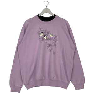 Peut inclure: Un sweat-shirt lavande avec un motif de oiseaux sur une branche de fleurs.