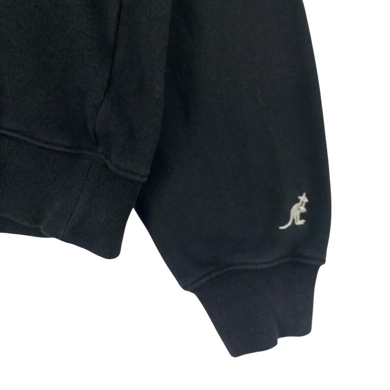 Puede incluir: Sudadera negra con pu&ntilde;os y dobladillo acanalados. Un peque&ntilde;o logotipo de canguro de color claro est&aacute; bordado en la manga. La prenda parece estar hecha de un material suave y c&oacute;modo.
