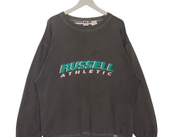 May include: A charcoal gray Russell Athletic sweatshirt with a crew neck and long sleeves. The front features the brand name in green and pink lettering. The sweatshirt is hanging on a white hanger.