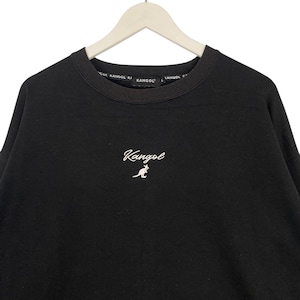May include: Black crew neck sweatshirt with the brand name "Kangol" embroidered in white script on the chest. The brand name is also printed around the neckline. The sweatshirt is hanging on a white hanger.