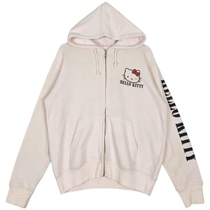 May include: Cream-colored zip-up hoodie featuring a Hello Kitty graphic with a red bow and the text "HELLO KITTY". The right sleeve displays the text "HELLO KITTY" in black. The hoodie has a hood and front pockets.