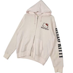 May include: Cream-colored zip-up hoodie featuring the Hello Kitty character with a red bow. The hoodie has a hood, a full-length zipper, and the words "HELLO KITTY" printed on the front and sleeve.